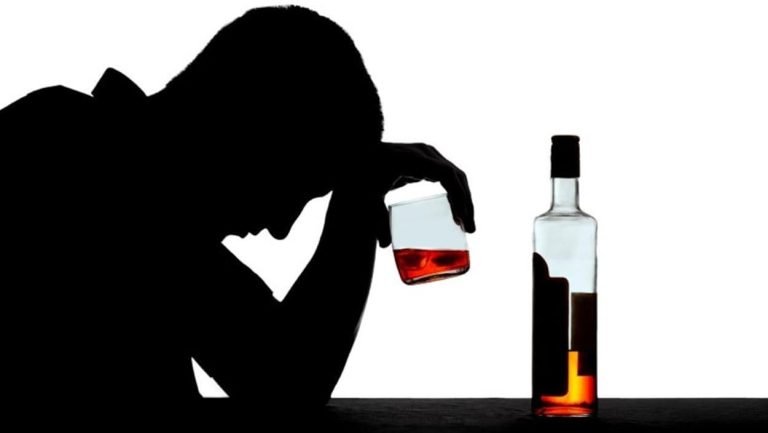 silhouette d'une personne alcoolique tenant un verre plein avec une bouteille posée sur une table